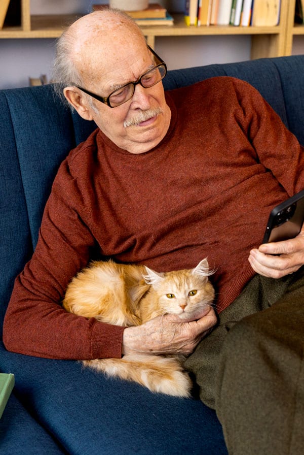 Un senior sur son téléphone avec son chat roux dans les bras